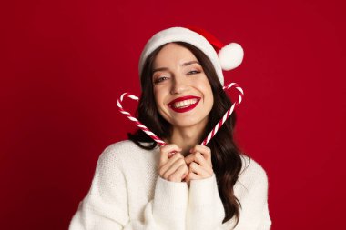 Kırmızı arka planda Noel Baba şapkası ve şeker kamışı olan güzel bir kadın. Noel sezonu