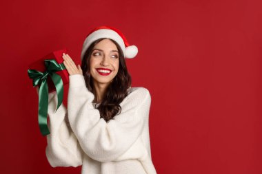 Kırmızı arka planda Noel Baba şapkası ve Noel hediyesi olan güzel bir kadın. Metin için boşluk