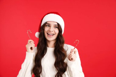 Kırmızı arka planda şeker kamışı olan, Noel Baba şapkalı ve kazaklı gülümseyen kadın, mesaj için yer. Mutlu Noeller ve mutlu yıllar.