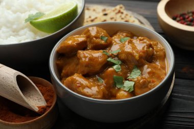 Lezzetli tavuk tikka masala, pilav, kişniş, kireç ve baharatlar ahşap masada, yakın plan.