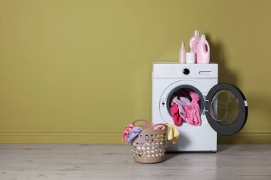 Modern çamaşır makinesi, deterjanlar ve zeytin duvarının yanındaki giysiler.