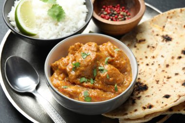 Lezzetli tavuk tikka masala, lavaş, kişniş, pirinç ve biberler gri masada, yakın plan.