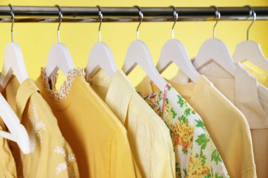 Sarı arka planda askıda asılı farklı şık kıyafetler, yakın plan.