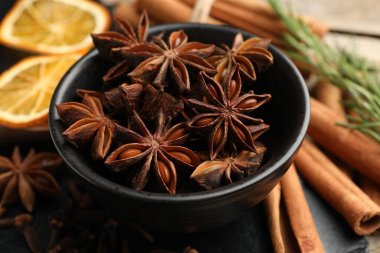 Sıcak şarap baharatları. Kasedeki anason yıldızları, tarçın çubukları, kuru portakal dilimleri ve masada taze biberiye, yakın plan.