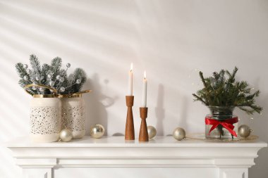 Beyaz duvarın yanındaki şöminede Noel süsü ve yanan mumlar.