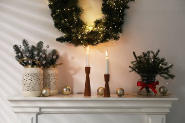 Beyaz duvarın yanındaki şöminede Noel süsü ve yanan mumlar.