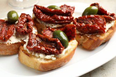 Krem peynirli lezzetli bruschettalar, güneşte kurutulmuş domatesler ve yeşil zeytinler masada, yakın plan.