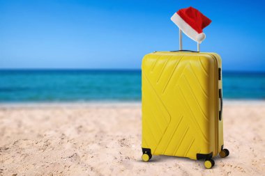 Noel tatili. Okyanus kıyısındaki kumlu sahilde Noel Baba şapkalı çanta.