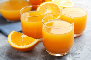 Taze portakal suyu ve meyveler gri masada, yakın plan.