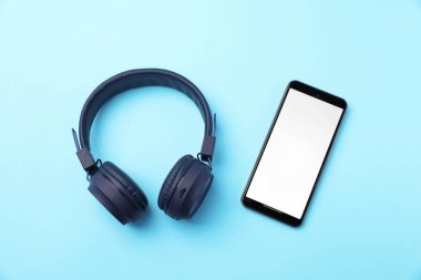 Şık kulaklıklar ve açık mavi arka planda akıllı telefon, düz konum