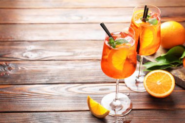 Glasses of refreshing spritzer cocktail and oranges on wooden table. Space for text