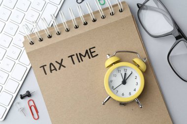 Vergi zamanı. Alarm saati, not defteri, gözlükler ve bilgisayar klavyesi masanın üstünde, üst görünümde