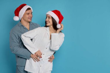 Açık mavi arka planda Noel Baba şapkalı ve pijamalı mutlu çift, mesaj için yer var. Noel atmosferi