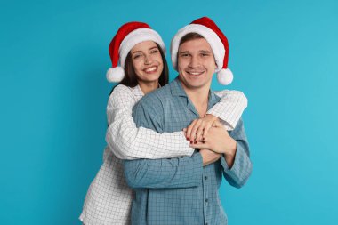 Açık mavi arka planda Noel Baba şapkalı ve pijamalı mutlu bir çift. Noel atmosferi