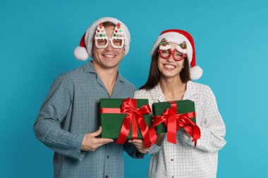 Noel Baba şapkalı ve pijamalı mutlu çift açık mavi arka planda Noel hediyeleri