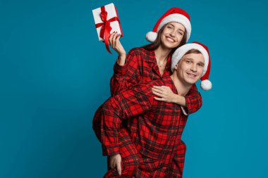 Noel Baba şapkalı ve pijamalı mutlu çift açık mavi arka planda Noel hediyesi, mesaj için yer var.