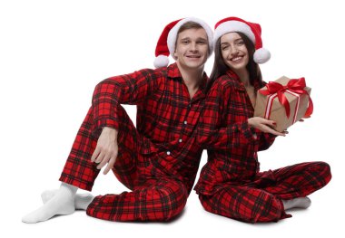 Noel Baba şapkalı ve pijamalı mutlu çift ve beyaz arka planda Noel hediyesi.