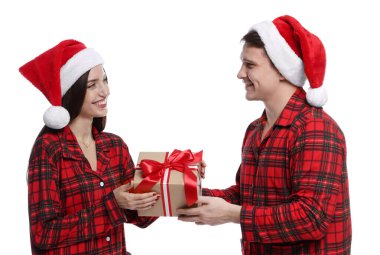 Noel Baba şapkalı ve pijamalı mutlu çift ve beyaz arka planda Noel hediyesi.