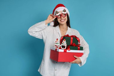 Noel Baba şapkalı ve pijamalı mutlu kadın. Açık mavi arka planda Noel hediyeleri.