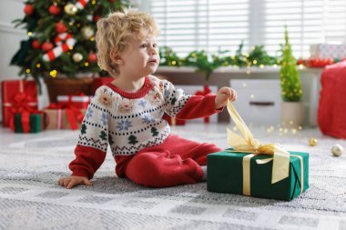 Noel hediyesi olan şirin bir bebek. Şenlikli bir odada yerde.