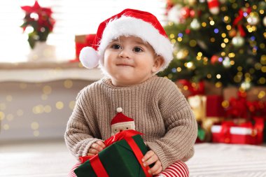 Evde yerde Noel Baba şapkası ve hediyesiyle küçük şirin bir bebek. Noel sezonu