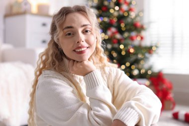 Evdeki bulanık ışıklara karşı süveter giymiş gülümseyen kadın portresi. Mutlu Noeller ve mutlu yıllar.