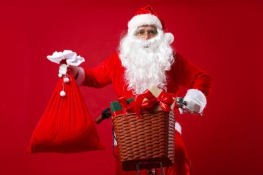Bisikletli Noel Baba ve çuval içinde Noel hediyeleri kırmızı arka planda