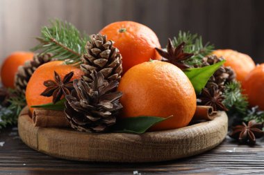 Olgun mandallar, baharatlar, köknar ağacı dalları ve tahta masanın üzerindeki koniler, yakın plan.