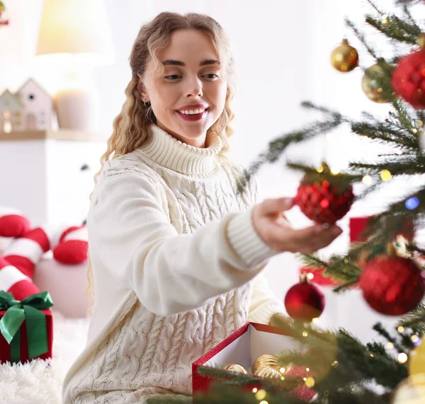 Evdeki Noel ağacına süveter giyen gülümseyen kadın güzel bir takı takıyor. Bokeh etkisi