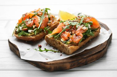 Somon, avokado, roka, tohumlar ve beyaz ahşap masada beyaz peynir, yakın plan.