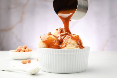 Lezzetli dondurmanın üzerine karamel sosu dökmek. Beyaz masada badem, yakın plan.