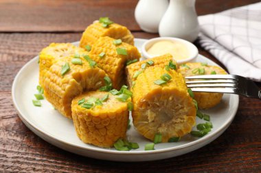 Haşlanmış mısır koçanları ve yeşil soğanlar ahşap masada servis ediliyor.