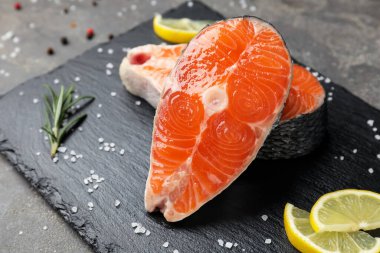 Pieces of salmon fillet with spices and lemon on gray table, closeup