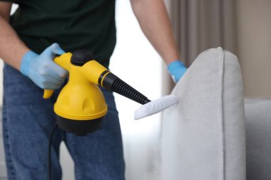 Haşere kontrol işçisi kanepeyi temizliyor. Kapalı alanda buhar temizleyicisi var.