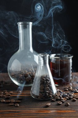 Kahve, fasulye ve beher dumanlı cam mataralar ahşap masada, yakın plan.