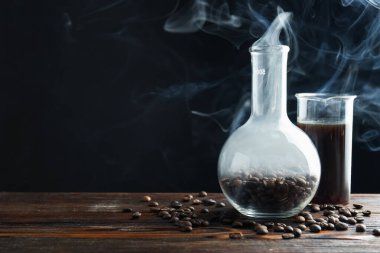 Kahve, fasulye ve beher dumanlı cam matara siyah arka planda, yakın plan. Metin için boşluk