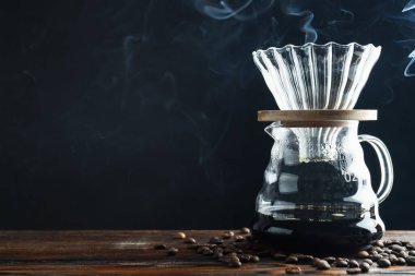 Kahve ve fasulye dumanlı cam kimya kahve makinesi, siyah arka planda, ahşap masada, yakın plan. Metin için boşluk