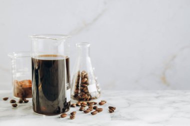 Lezzetli kahve, fasulye ve pudra ile laboratuvar bardakları beyaz mermer masada, yakın plan. Metin için boşluk