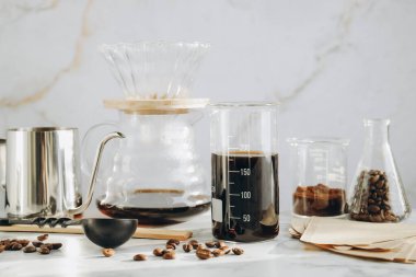 Lezzetli kahve, fasulye, bardaklar, çaydanlık, kağıt filtreler ve beyaz mermer masa üzerinde kimya kahve makinesi.