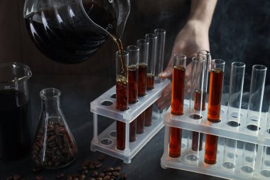 Siyah masada cam test tüpüne damlatan kadın, yakın plan.