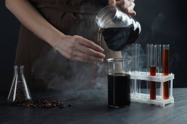 Siyah masada cam test tüpüne damlatan kadın, yakın plan.