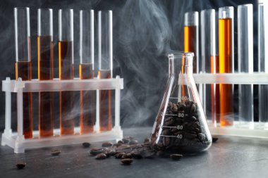 Kahve, fasulye ve dumanlı laboratuvar bardakları siyah masada, yakın plan.