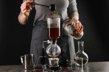 Gri masada vakumlu kahve makinesiyle kahve yapan kadın, yakın plan.