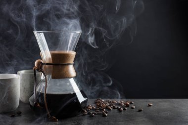 Cam kimya kahve makinesi, lezzetli kahve, fasulye ve fincanlar gri masada, yakın plan. Metin için boşluk