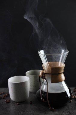 Cam kimya kahve makinesi, lezzetli kahve, fasulye ve fincanlar gri masada, yakın plan.