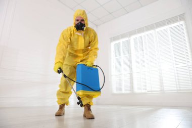 Koruyucu giysiler içinde böcek ilacı sıkan bir haşereci. Düşük açılı. Metin için boşluk