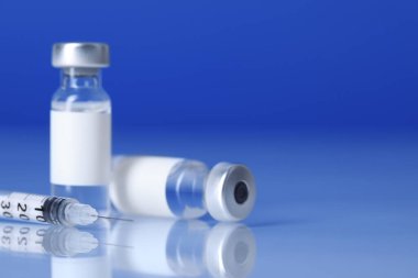 Işık ayna yüzeyinde mavi arka plana karşı şırınga ve tüplerde aşı, yakın plan. Metin için boşluk