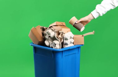 Yeşil arka planda çöp kutusuna çöp atan kadın, yakın plan. Atık sıralama