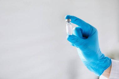 Hemşire arka planda aşı şişesi tutuyor, yakın plan. Metin için boşluk