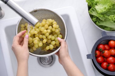 Mutfakta elek üzümleri yıkayan bir kadın.